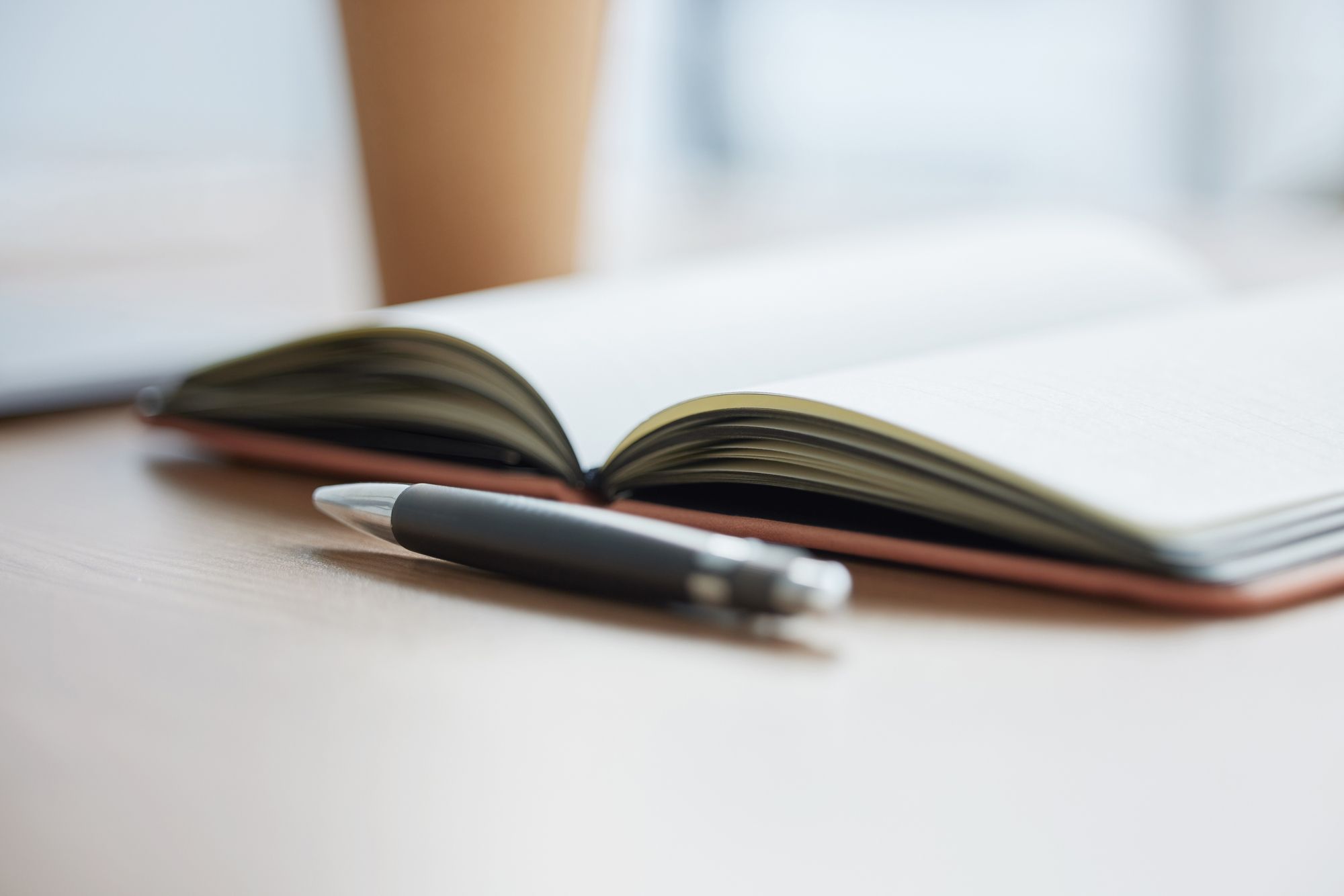 Aufgeschlagenes Notizbuch mit Kugelschreiber auf einem Schreibtisch.