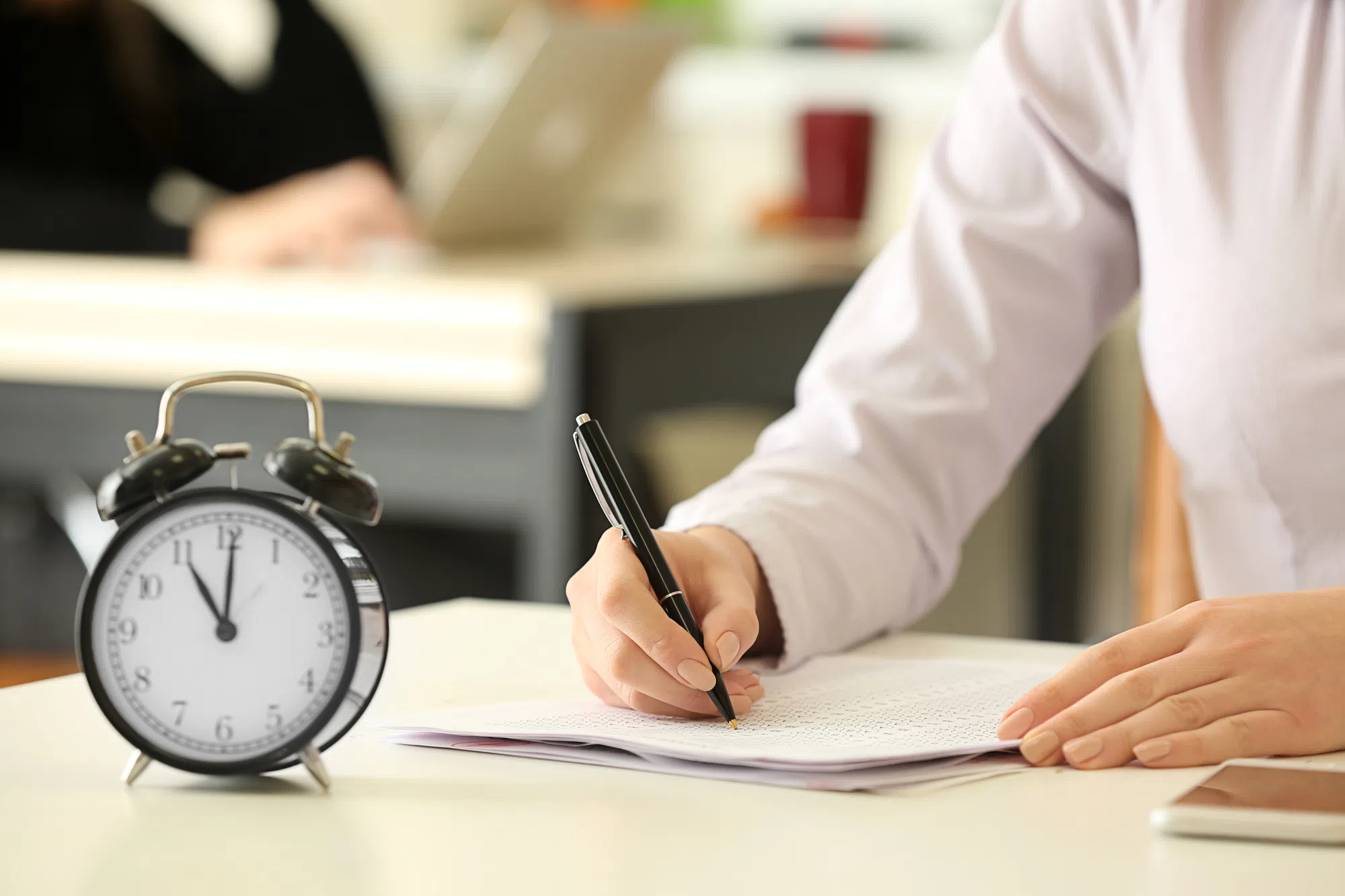 Frau unterschreibt Dokumente neben einem Wecker.